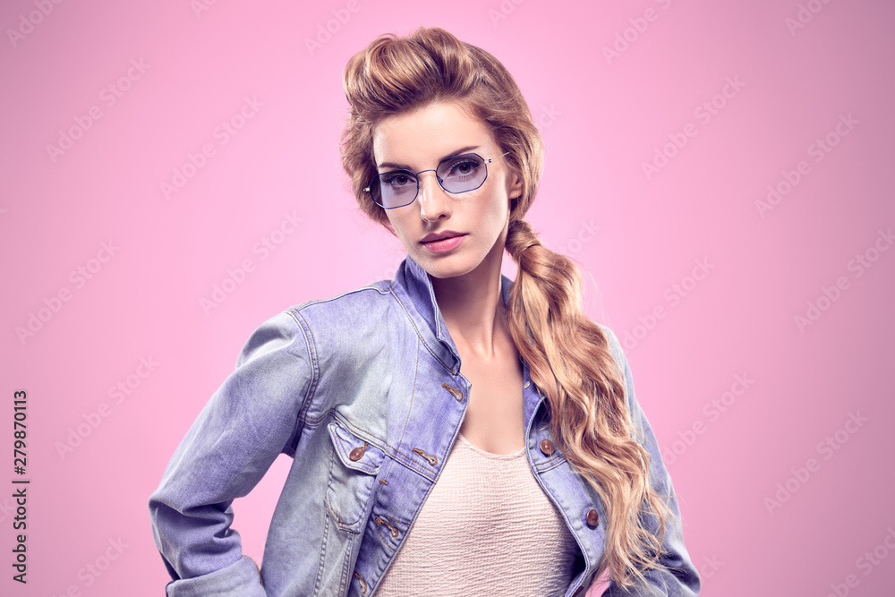 Fashion. Gorgeous long-haired blonde woman in Stylish denim jacket. Glamour Lady in Trendy Outfit, blue Sunglasses. Beautiful fashionable Model Girl with trendy hairstyle, makeup in Studio on Pink Fashion. Gorgeous long-haired blonde woman in Stylish denim jacket. Glamour Lady in Trendy Outfit, blue Sunglasses. Beautiful fashionable Model Girl with trendy hairstyle, makeup in Studio on Pink