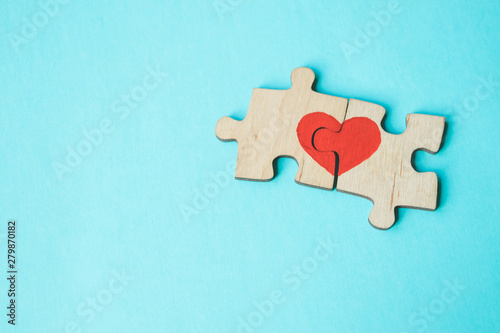 Red heart is drawn on the pieces of the wooden puzzle lying next to each other on blue background. Love concept. St. Valentine day. Copy space.