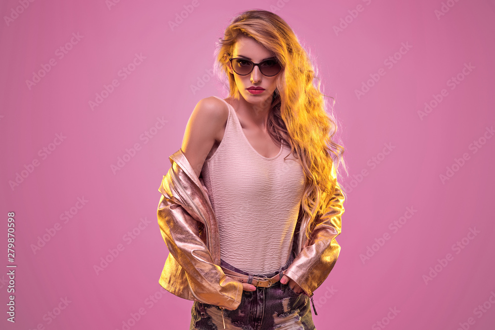 High Fashion neon. Gorgeous Blond woman wearing Stylish gold jacket and  Sunglasses. Glamour sexy long-haired Model Girl, makeup in Trendy Outfit,  neon light. Creative Bright Color fashionable Portrait foto de Stock |