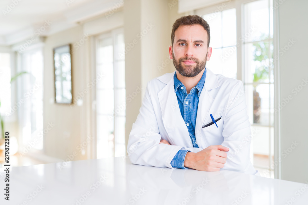 Handsome doctor man wearing medical coat at the clinic Relaxed with serious expression on face. Simple and natural looking at the camera.