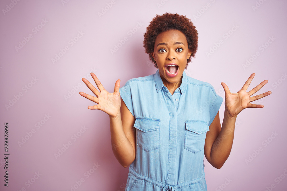 Young beautiful african american woman with afro hair over isolated pink background celebrating crazy and amazed for success with arms raised and open eyes screaming excited. Winner concept Young beautiful african american woman with afro hair over isolated pink background celebrating crazy and amazed for success with arms raised and open eyes screaming excited. Winner concept