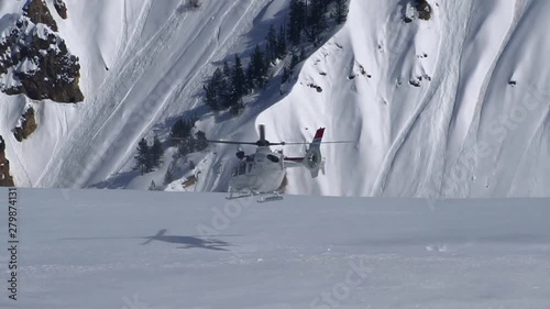 A luxurious white helicopter takes off in the Alpine mountains in winter. Active sports were dropped by a helicopter on top of the mountain. In the background is a mountain range covered in snow.