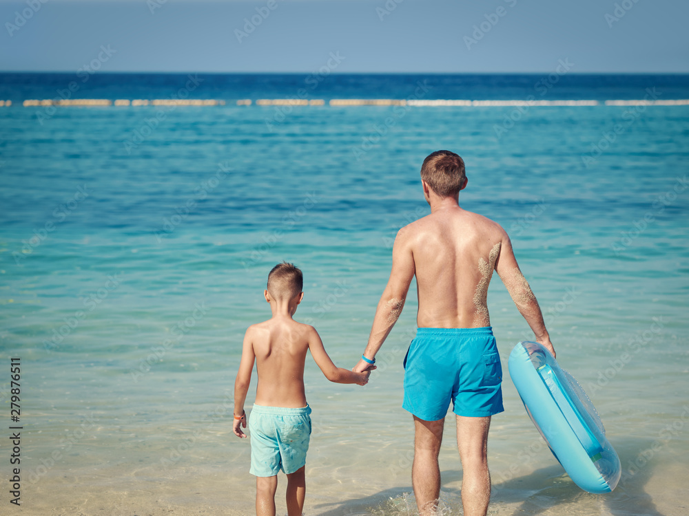 Father and son spending time together on sea beach on summer vacation.