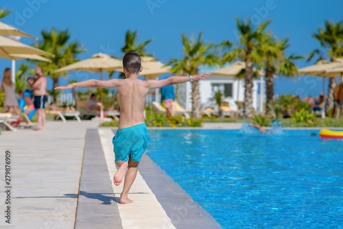 Smiling Caucasian boy having fun in swimming pool at resort on family vacation. He is running along pool edge. © Artem