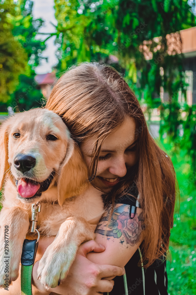 The young woman walks with the little dog in the park. Golden retriever.