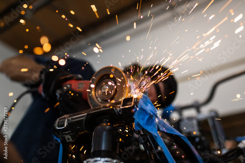 Worker cutting, grinding and polishing motorcycle metal part with sparks indoor workshop, close-up. photo