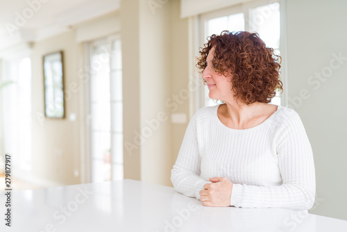 Beautiful senior woman wearing white sweater at home looking to side, relax profile pose with natural face with confident smile.