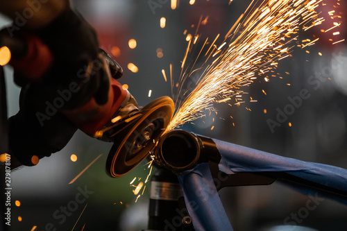 Worker cutting, grinding and polishing motorcycle metal part with sparks indoor workshop, close-up. photo