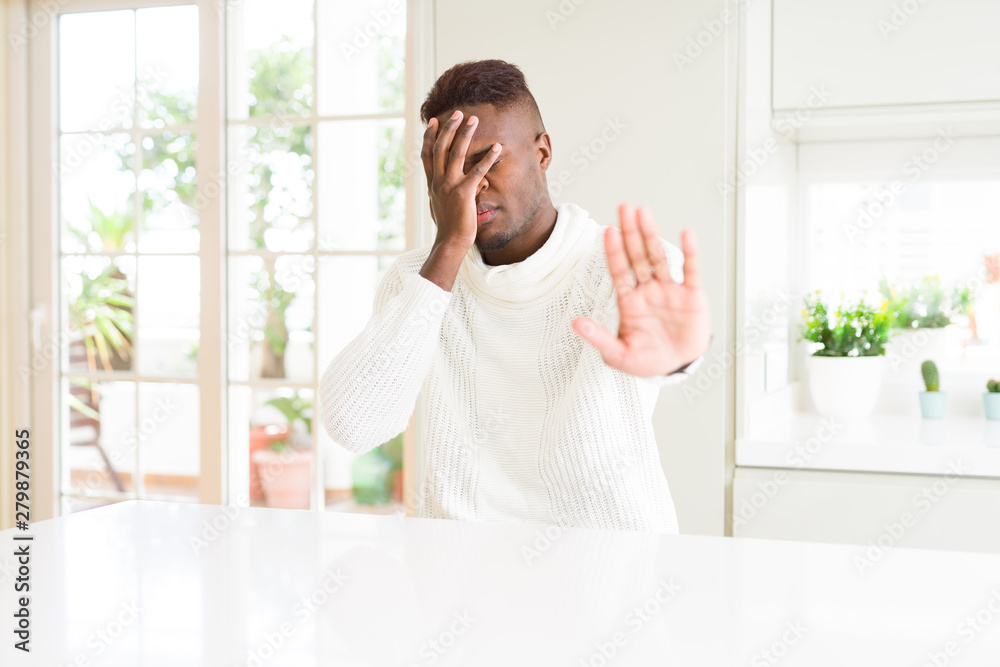 Handsome african american man on white table covering eyes with hands and doing stop gesture with sad and fear expression. Embarrassed and negative concept.