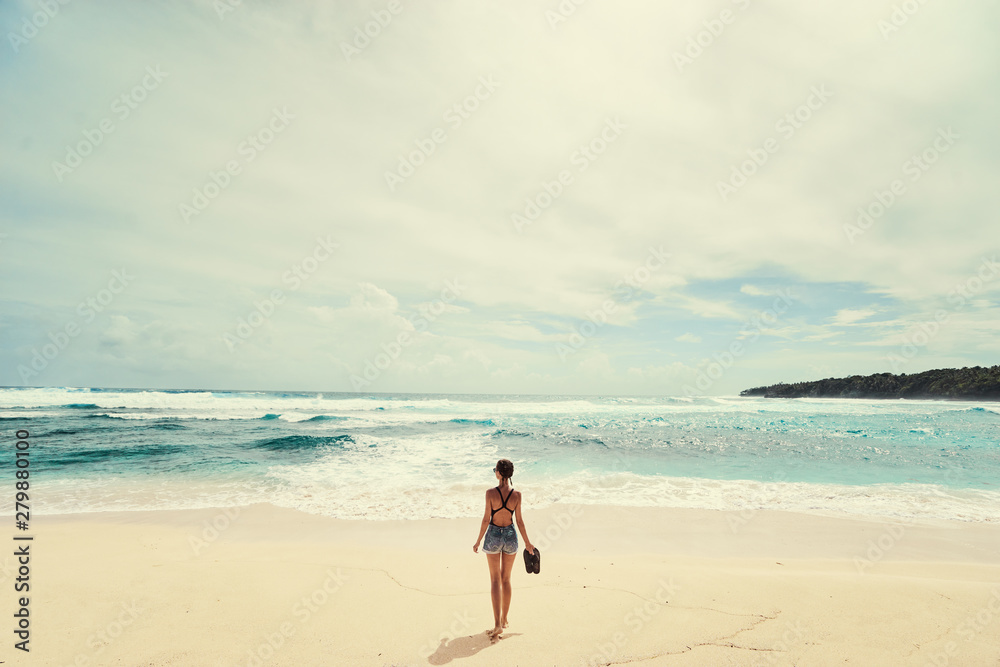 Vacation on the shore. Young woman standing on tropical beach enjoying beautiful view.