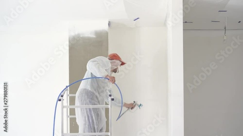 repair of the apartment - professional painter paints the walls with white paint spray gun