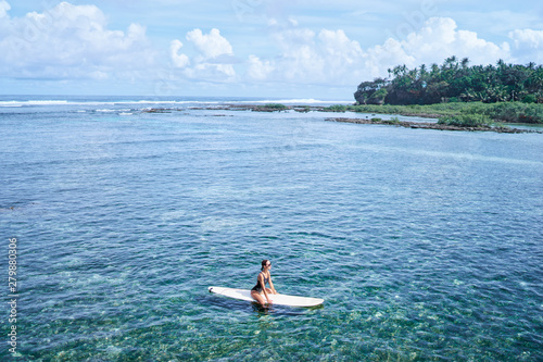 Hobby and vacation. Young woman swimming over surfboard in clear blue water at beach, Siargao Island, Philippines.