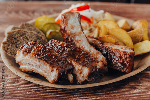 Delicious beef ribs with sauce, fried potatoes, cucumber, cabbage and khlobe in a paper plate on a wooden table. takeaway street food