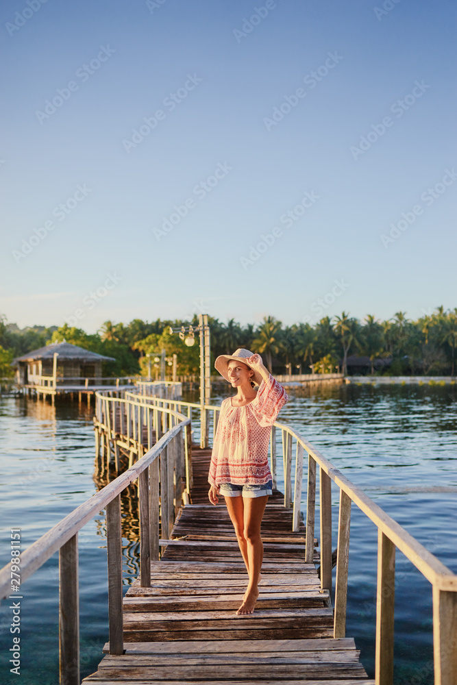 Fototapeta premium Vacation on tropical island. Young woman in hat enjoying sunset sea view from wooden bridge terrace, Siargao Philippines.