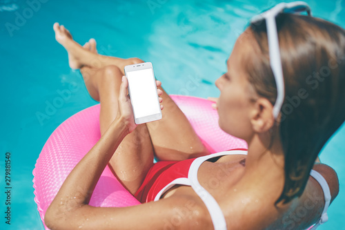 Vacation and technology. Young woman using smartphone at swimming pool. Copy space on the screen.