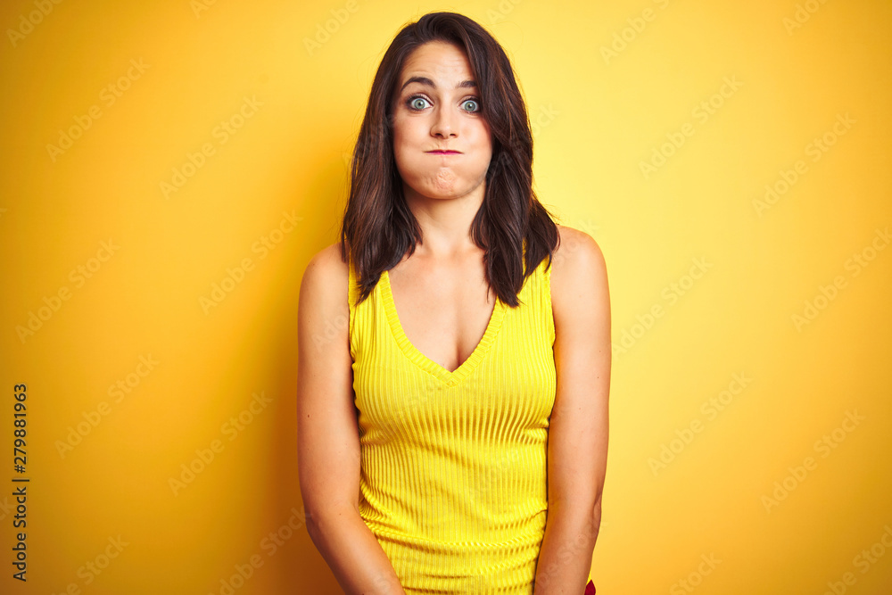 Young beautiful woman wearing t-shirt standing over yellow isolated background puffing cheeks with funny face. Mouth inflated with air, crazy expression. Young beautiful woman wearing t-shirt standing over yellow isolated background puffing cheeks with funny face. Mouth inflated with air, crazy expression.