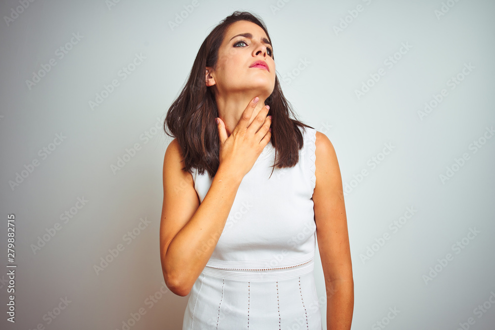 Young beautiful woman wearing dress standing over white isolated background Touching painful neck, sore throat for flu, clod and infection Young beautiful woman wearing dress standing over white isolated background Touching painful neck, sore throat for flu, clod and infection
