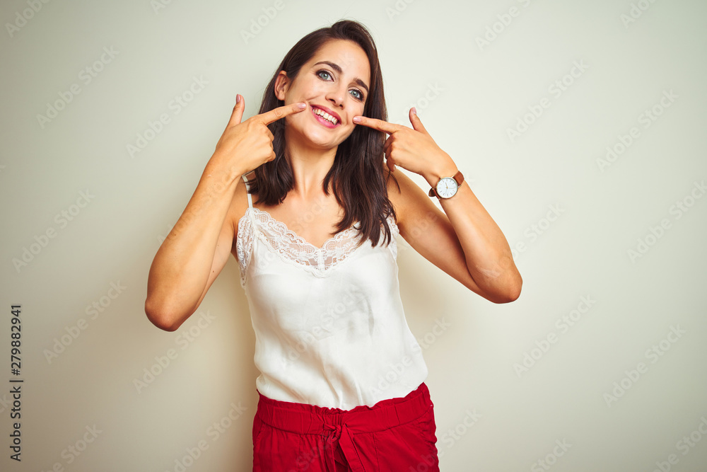 Young beautiful woman wearing t-shirt standing over white isolated background smiling cheerful showing and pointing with fingers teeth and mouth. Dental health concept.