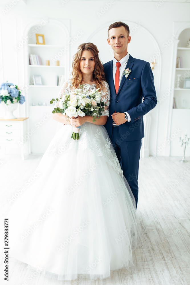 Beautiful bride in white dress and groom in suit, posing in white Studio interior, wedding Beautiful bride in white dress and groom in suit, posing in white Studio interior, wedding