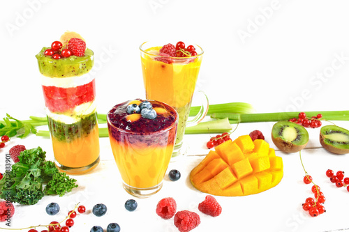Wielowarstwowe smoothie w szklankach wokół rozsypanych owoców