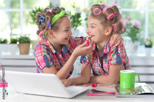 Cute twin girls in hair curlers with laptop