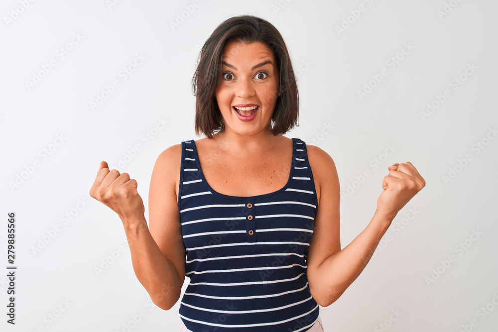 Young beautiful woman wearing blue striped t-shirt standing over isolated white background celebrating surprised and amazed for success with arms raised and open eyes. Winner concept. Young beautiful woman wearing blue striped t-shirt standing over isolated white background celebrating surprised and amazed for success with arms raised and open eyes. Winner concept.