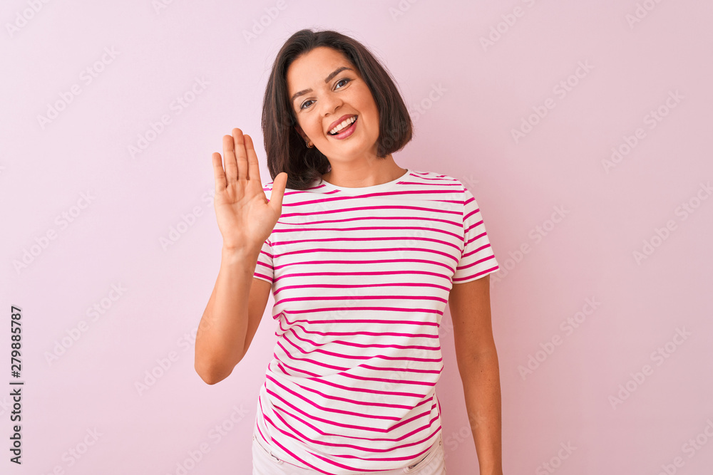Young beautiful woman wearing striped t-shirt standing over isolated pink background Waiving saying hello happy and smiling, friendly welcome gesture Young beautiful woman wearing striped t-shirt standing over isolated pink background Waiving saying hello happy and smiling, friendly welcome gesture