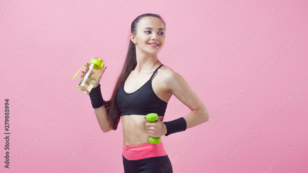Portrait of an attractive girl, cute, with a tight-fitting uniform, with dumbbell in one hand and a bottle in the other. Portrait of an attractive girl, cute, with a tight-fitting uniform, with dumbbell in one hand and a bottle in the other.