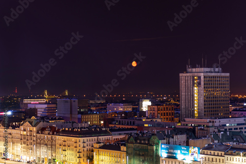 Warsaw in the light of night lights and red moon