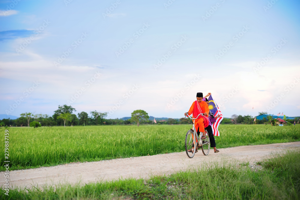 independence Day concept - Two happy young local boy riding old bicycle at paddy field holding a Malaysian flag
