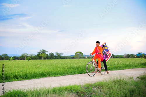independence Day concept - Two happy young local boy riding old bicycle at paddy field holding a Malaysian flag