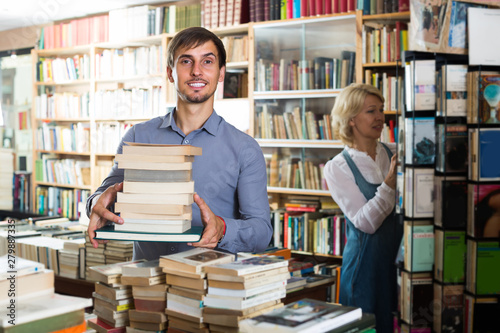 man with pile of book in book store.