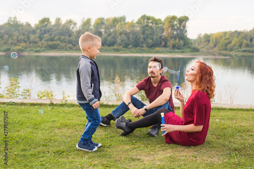 Family and nature concept - Mother, father and their child playing with colorful soap bubbles
