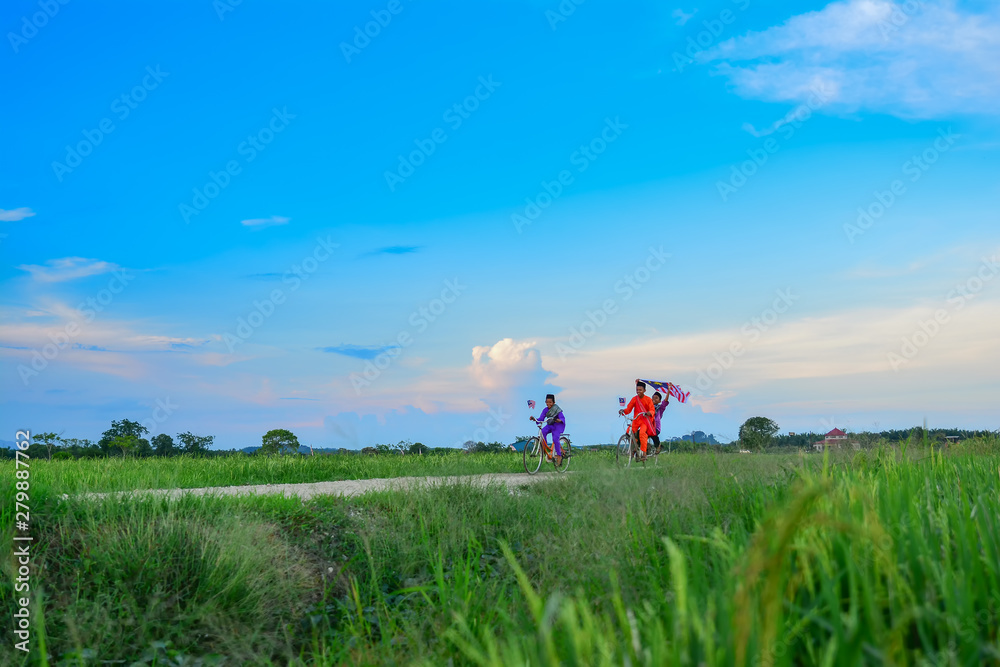 independence Day concept - Two happy young local boy riding old bicycle at paddy field holding a Malaysian flag independence Day concept - Two happy young local boy riding old bicycle at paddy field holding a Malaysian flag