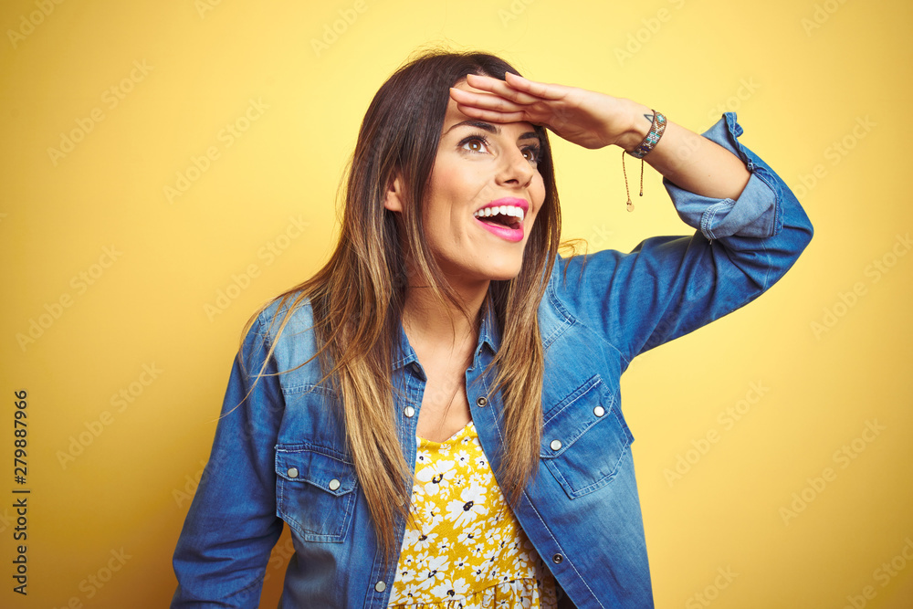 Young beautiful woman standing over yellow isolated background very happy and smiling looking far away with hand over head. Searching concept. Young beautiful woman standing over yellow isolated background very happy and smiling looking far away with hand over head. Searching concept.