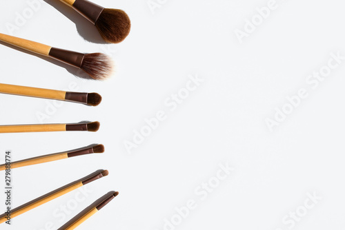 Top view of make up brushes set, arranged in a line. Natural accessories with bamboo wood handles. Copy space on white table.