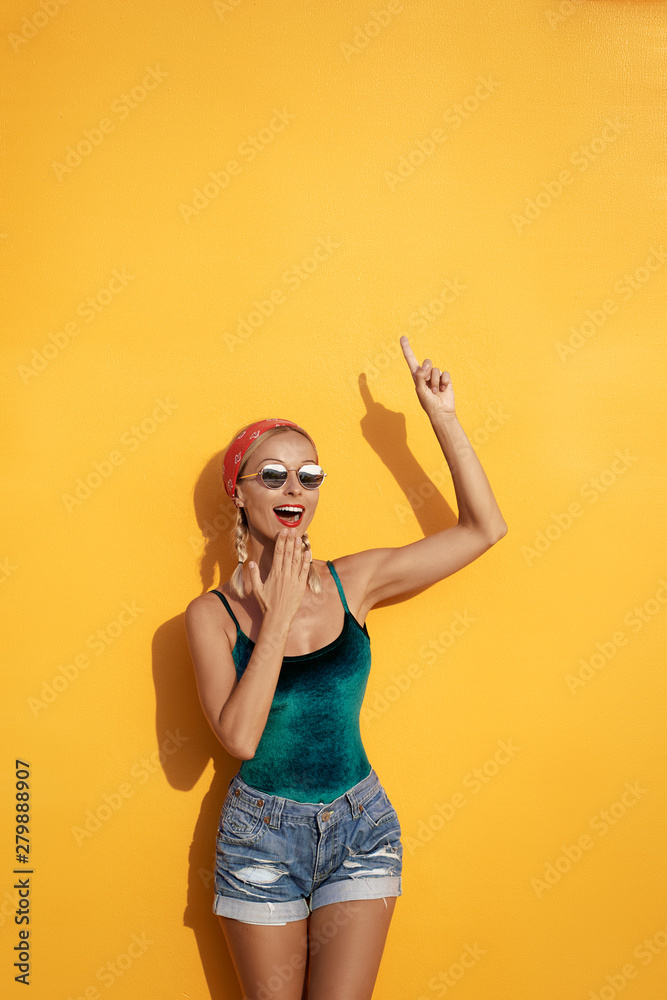 Your text here. I have an idea!Amazed beautiful young woman pointing up while standing against yellow wall.