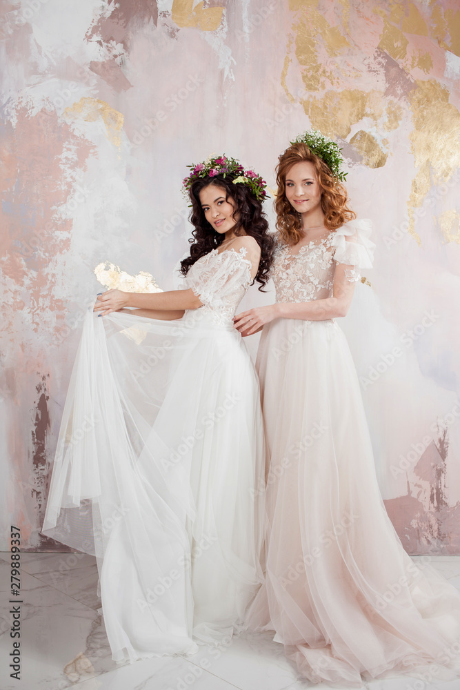 Two charming brides in beautiful spring wreaths on their heads. Beautiful young women in wedding dresses Two charming brides in beautiful spring wreaths on their heads. Beautiful young women in wedding dresses
