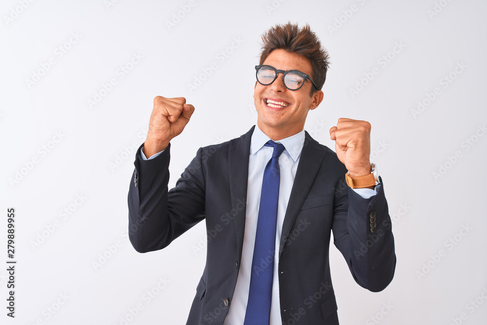 Young handsome businessman wearing suit and glasses over isolated white background very happy and excited doing winner gesture with arms raised, smiling and screaming for success. Celebration concept. Young handsome businessman wearing suit and glasses over isolated white background very happy and excited doing winner gesture with arms raised, smiling and screaming for success. Celebration concept.