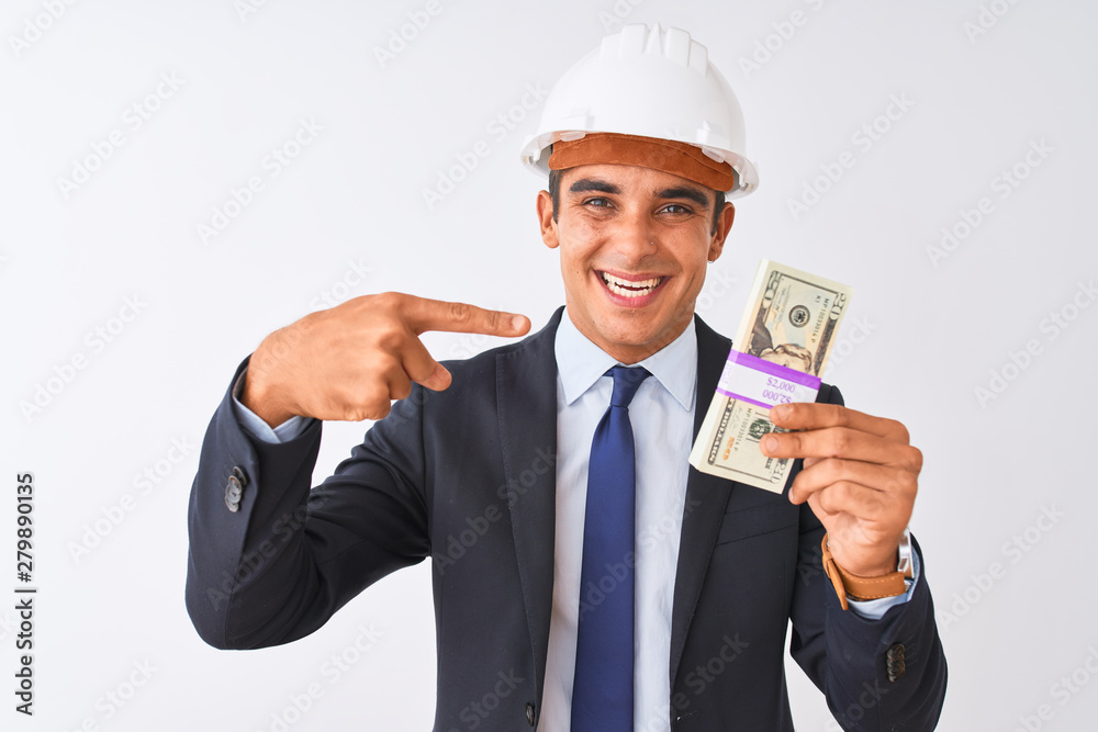 Young handsome architect man wearing helmet holding dollars over isolated white background very happy pointing with hand and finger
