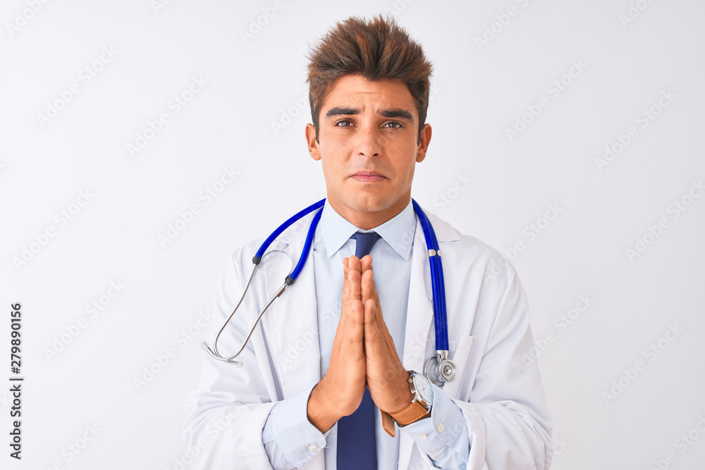 Young handsome doctor man wearing stethoscope over isolated white background begging and praying with hands together with hope expression on face very emotional and worried. Asking for forgiveness. Young handsome doctor man wearing stethoscope over isolated white background begging and praying with hands together with hope expression on face very emotional and worried. Asking for forgiveness.