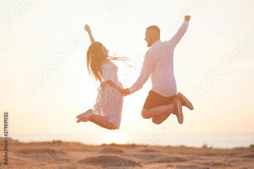 young and free loving caucasian couple jumping male and female holding hands outdoor leisure on summer sea sunset