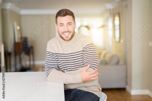Young handsome man wearing a sweater at home happy face smiling with crossed arms looking at the camera. Positive person.