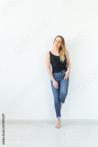 Style and people concept - young woman in jeans standing over the white wall and looks like sexy