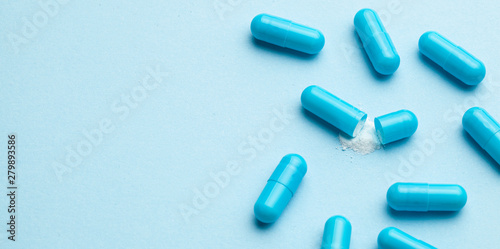 Blue tablets in capsules. One capsule is open. Blue background. Copy space for text.