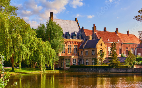 Vintage building over lake of love in Minnewater park in Bruges Belgium near Beguinage monastery of Beguines. Picturesque landscape with green trees sunset time.