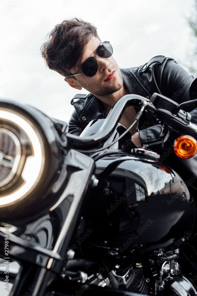 selective focus of handsome motorcyclist in leather jacket looking away while sitting on motorcycle selective focus of handsome motorcyclist in leather jacket looking away while sitting on motorcycle