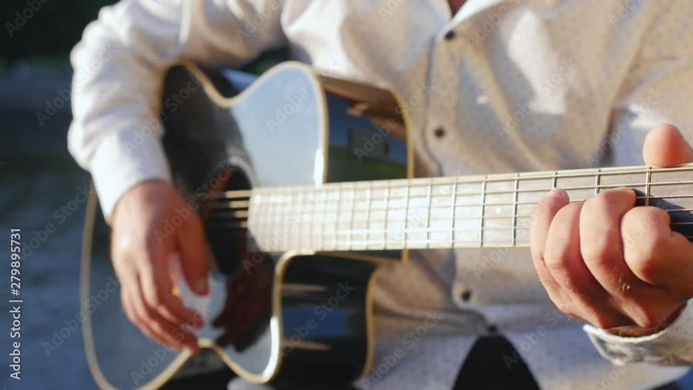Man hands plays guitar against the lake. Guitarist touching guitar strings. Close up shot. Man hands plays guitar against the lake. Guitarist touching guitar strings. Close up shot.