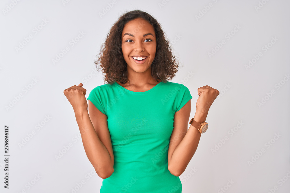 Young brazilian woman wearing green t-shirt standing over isolated white background celebrating surprised and amazed for success with arms raised and open eyes. Winner concept. Young brazilian woman wearing green t-shirt standing over isolated white background celebrating surprised and amazed for success with arms raised and open eyes. Winner concept.