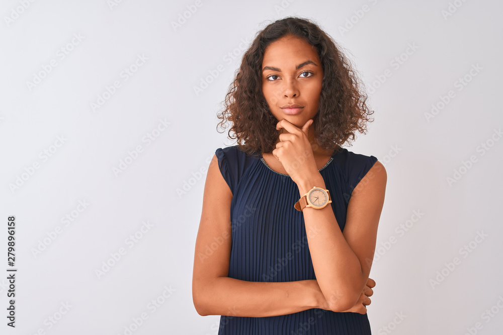 Young brazilian woman wearing blue dress standing over isolated white background looking confident at the camera with smile with crossed arms and hand raised on chin. Thinking positive.